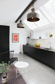 Monolithic kitchen counter with black fronts below strip of skylights and metal, industrial-style pendant lamps