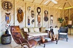 Vintage leather rocking chair and rattan sofa set in lounge amongst handcrafted artworks hanging on wooden wall