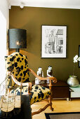 Elegant armchair with animal print cover, Oriental china figurines and orchid in silver pot below framed drawing