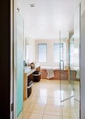 Blick in Badezimmer mit beigen Bodenfliesen; Wäschekörben unter Steinwaschtisch und halboffene Duschtür