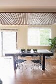 Sunny dining area with black table and wire chairs with seat cushions below suspended ceiling