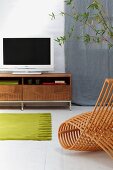 Modern chair made from bent wooden slats in front of green rug on white tiled floor and flat-screen TV on lowboard