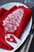 Festive place setting with glass fir cone and paper tag on red linen napkin