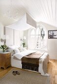 Bed with upholstered headboard and canopy in attic room with arched window and white wooden ceiling