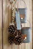 Pinienzapfen mit weihnachtlichen Bändern und Windlichter hängen auf Haken an einer Holzwand