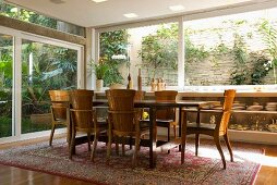 Dining table and armchairs in traditional Mediterranean style on classic Oriental rug in front of large windows running round two sides of room
