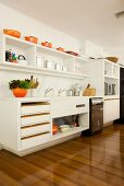 Pans and casseroles in cheerful orange bring colour to white modern kitchen with glossy parquet flooring