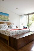 Double bed with floral bed linen and wide trunk of exotic wood in bedroom with open sliding door