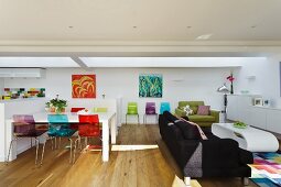 Colourful plastic chairs at white dining table next to lounge area with black couch in open-plan living space