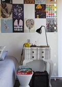 Detail of bedroom with modern stool in front of vintage bedside table against wall below collection of posters