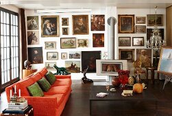 Large gallery of oil paintings in living room with orange couch, antiques, crystal chandelier and log burner