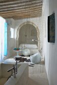 Stone bathtub in ensuite bathroom; thread curtain as partition between seating area with designer furniture and bed in Oriental alcove