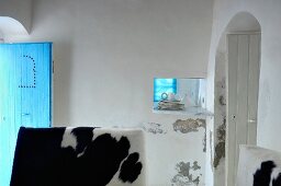 Raum mit einer blauen und einer weissen geöffneten Holztür; Tierfelle auf Möbeln im Vordergrund
