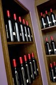 Dark wine bottles with red foil capsules in wood-clad niches in wall painted lilac