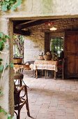 View through open doorway; vintage, terracotta veranda floor and baskets on table in front of barred window opening in stone wall