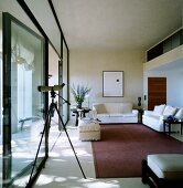 Purist interior with seating area on matte rug next to glass wall and telescope in foreground