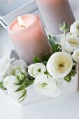 weiße Ranunkelblüten und brennende Kerzen in weisser schale