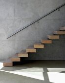 Floating wooden stair treads on exposed concrete wall and stainless steel handrail
