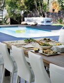 Chairs with white leather covers at set table in garden with view of pool