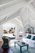 Light-flooded living room of beach house with wooden pavilion roof and magnificent view of rocky coast