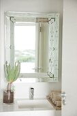 Badezimmerspiegel mit sich darin spiegelnder Landschaft; auf dem Waschbecken eine Sukkulente in einer Glasvase