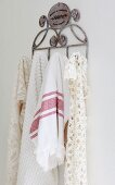 Tea towel and lacy cloths hanging from metal hooks on white wall