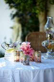 Table set with oil lamp, tealight holders, flowers and jug of lemonade