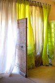 Airy curtains in various shades of green and open, rustic wooden door
