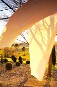 Pergola with wafting curtain and patterns of light and shadow in front of Mediterranean landscape