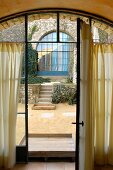 View through open French window into courtyard terrace with blue, arched lattice window on far side