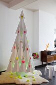 Stylised Christmas tree made from white cardboard with decorations in neon yellow and pink on white fur rug