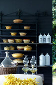 Ceramic containers and white porcelain containers on shelves in front of a black, patio wall