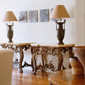 Urn table lamps on stone top console tables with ornate metal bases and modern metalwork on the wall