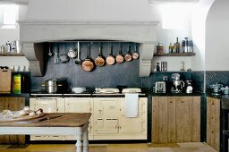 Antiker Küchentisch mit Schneidebrett vor Vintage Kochzeile und aufgehängter Kupferpfannen Sammlung in gemauertem Dunstabzugsbereich