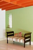 Orange-painted, wood-beamed ceiling above recamier against green wall