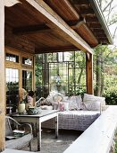 Cozy corner of a country home veranda with day bed and pillows in front of a stained glass wall and a view of trees