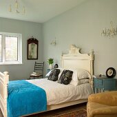 Schlafzimmer mit Textilmix auf antikem, weiss lackiertem Holzbett und taubenblauen Nachtkästchen unter Kristallleuchtern