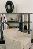 Pale armchair in front of half-height bookcase holding books and objet