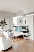 Double bed against partition and elegant, white leather armchair in open-plan bedroom