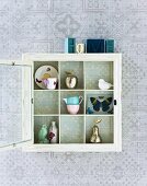 White lacquer, display cabinet hanging on a wallpapered wall with open glass door and view of the nick-nacks