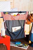 Stoffbehang mit aufgenähten Taschen zur Aufbewahrung von Spielsachen am Bettgestell eines Kinderzimmers