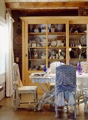 Chairs with fabric draped on backs around dining table in front of dresser full of crockery