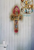 Chandelier and kitsch version of Christian cross on wood-clad wall above toilet