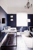 Home Office im Schlafzimmer - moderner Schreibtisch, Acryglas-Stuhl und Tischlampe vor eleganter, blauweiss gestalteter Wand