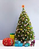 Roter Pouf, Geschenkpäckchen und Dekotiere unter einem mit allerlei Figürchen behängten Weihnachtsbaum
