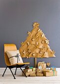 Stilisierter Weihnachtsbaum aus Packpapier-Dreiecken und Papier Weihnachtsschmuck an grauer Wand davor Weihnachtspäckchen