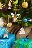 Blaue und grüne Geschenkpäckchen vor Weihnachtsbaum mit verschiedenen farbenfrohen Figürchen