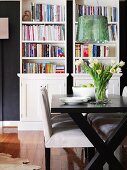 Lustrous green designer lamp above modern, black and white dining set; bookcases in background against dark wall