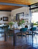 Delicate metal chairs around rustic dining table with collection of glass vessels used as planters in simple interior