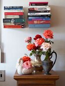 Rosensträusse in Metallkrügen und Porzellan Schwanfigur auf halbhohem Schränkchen unter Bücherstapel auf minimalistischen Konsolen an Wand